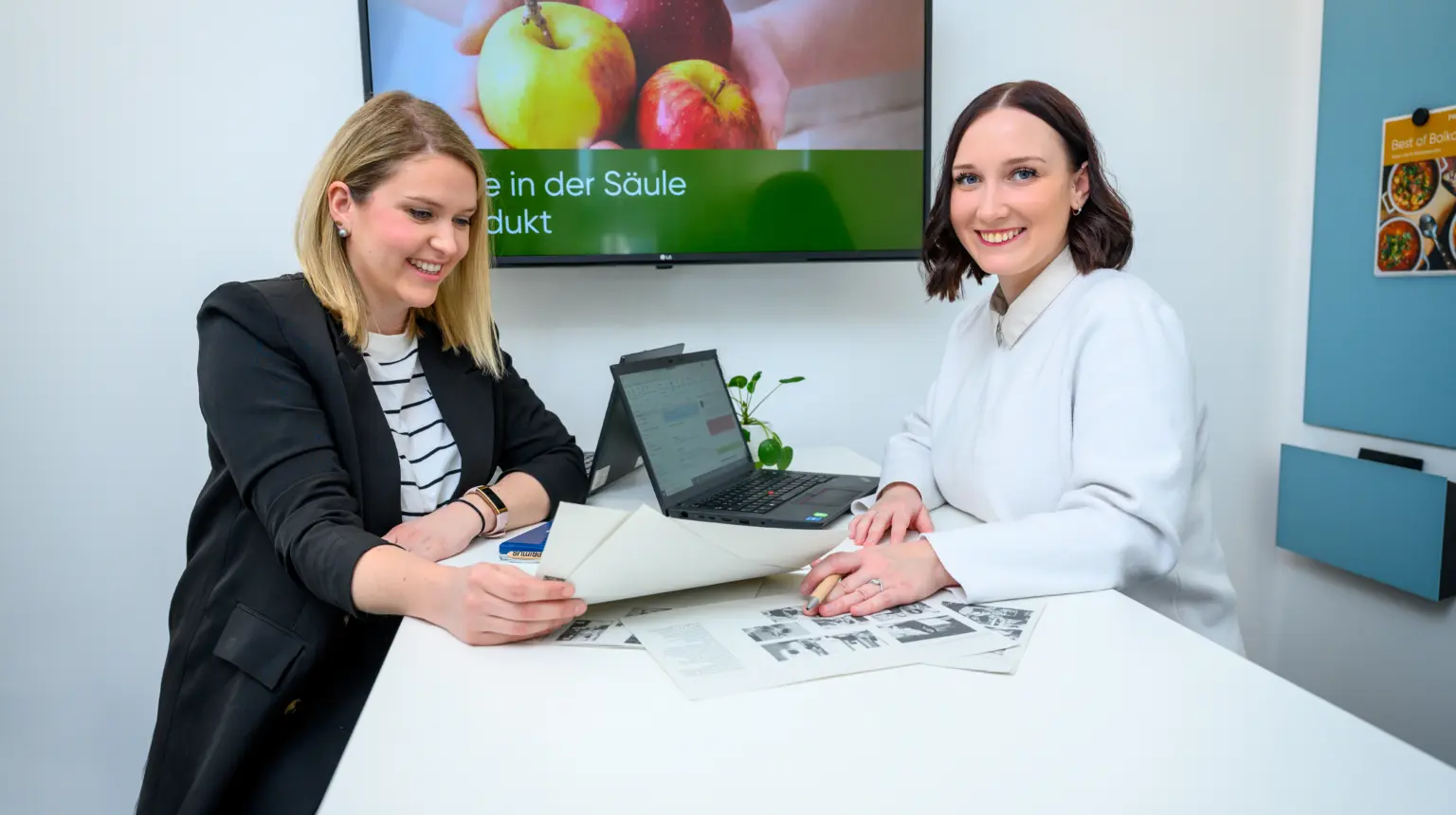 Manou und eine Kollegin sitzen sich an einem Tisch in einem Besprechungsraum gegenüber und führen ein Gespräch.
