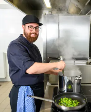 Mann kocht mit frischen Lebensmitteln bei Primus in einem Suppentopf