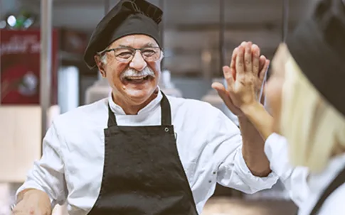 Älterer Koch und junge Köchin klatschen sich ab